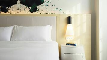 A hotel room with a bed, a wall-mounted lamp, and a small table with books.