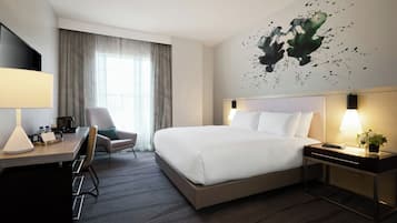 Una habitación de hotel con cama, escritorio, silla y un cuadro en la pared.
