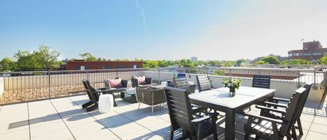 A rooftop terrace with a table and chairs, a small garden area, and a view of the cityscape.