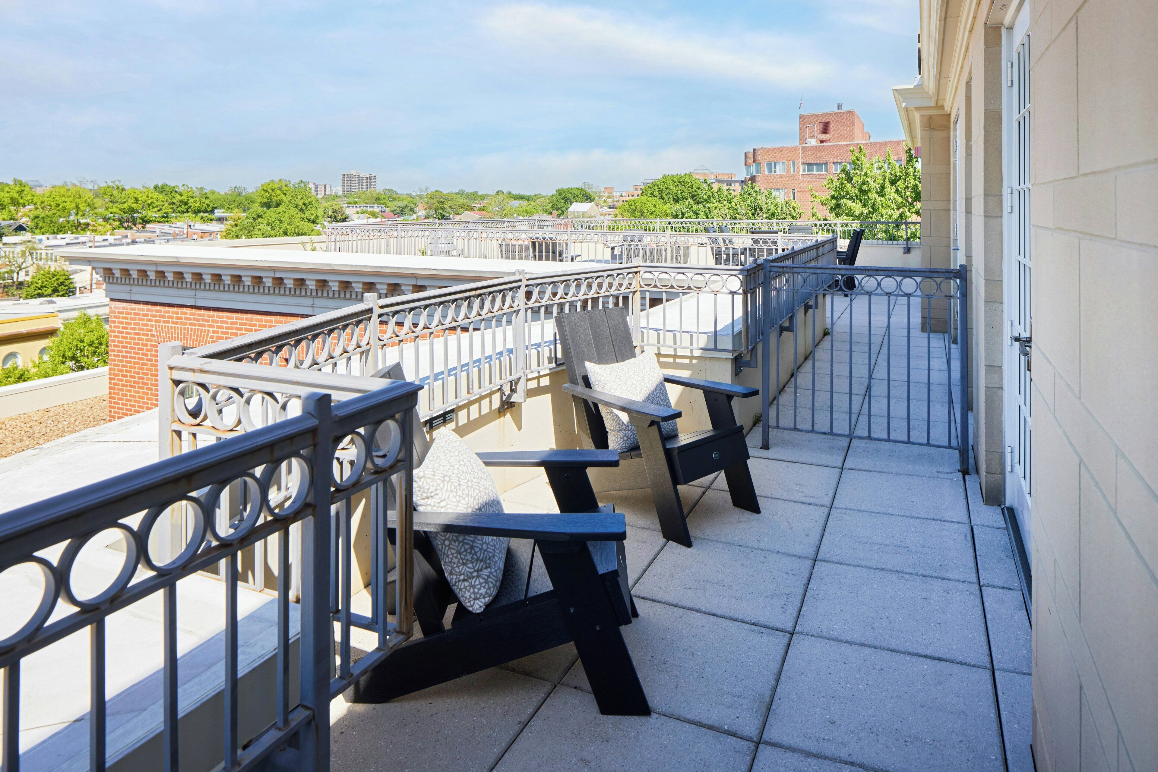 A balcony with outdoor seating, a metal railing, and a view of buildings and trees.