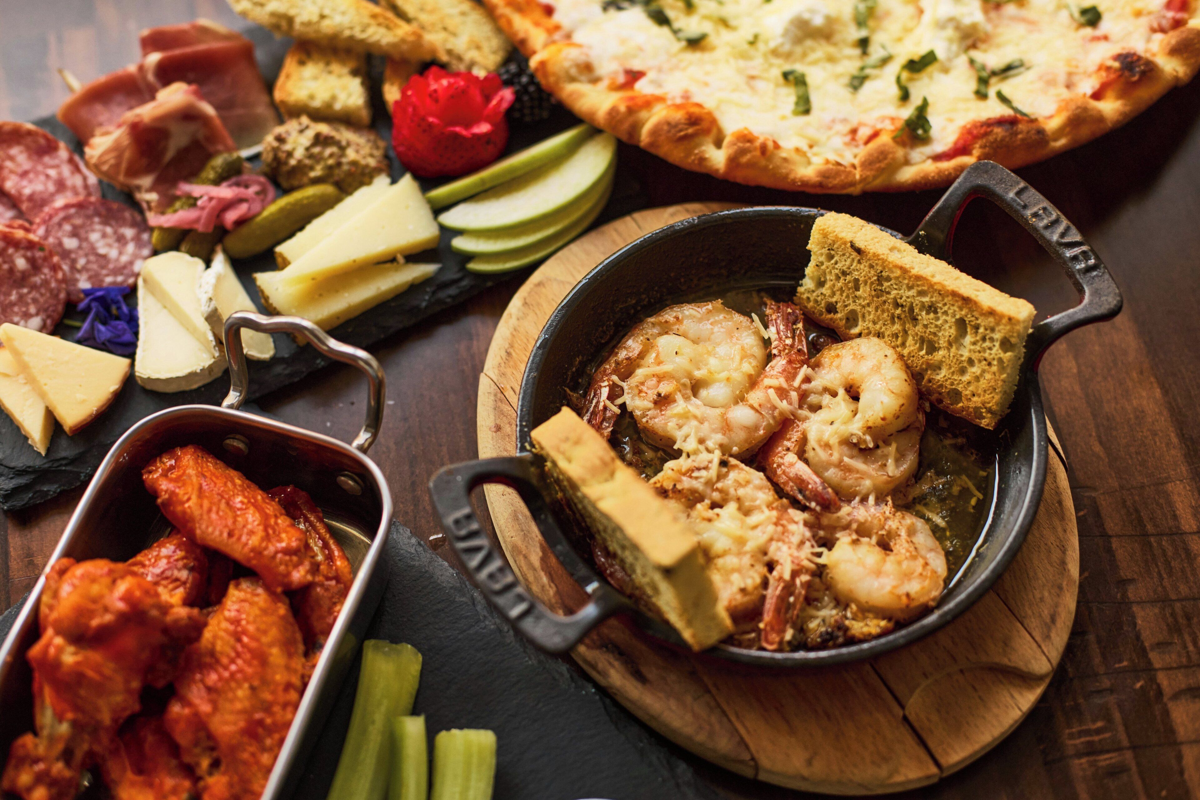 Une variété de produits alimentaires, notamment des crevettes, des ailes de poulet, du fromage et une pizza.