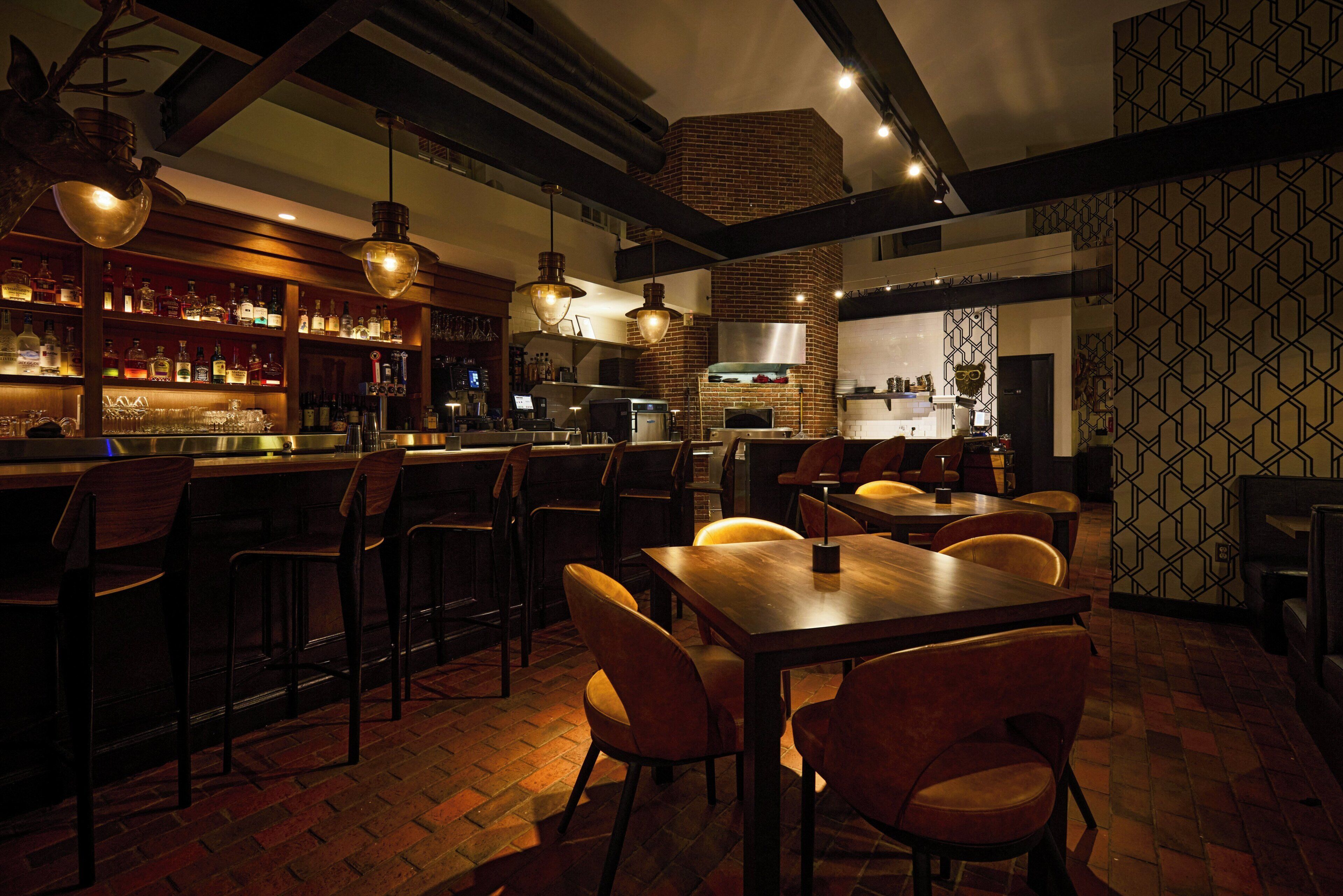 A bar area with wooden chairs, a long table, and hanging pendant lights.