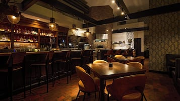 A bar area with wooden chairs, a long table, and hanging pendant lights.