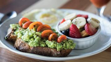 A plate with toast topped with guacamole and tomatoes, a bowl of mixed berries, and a glass of a red beverage.