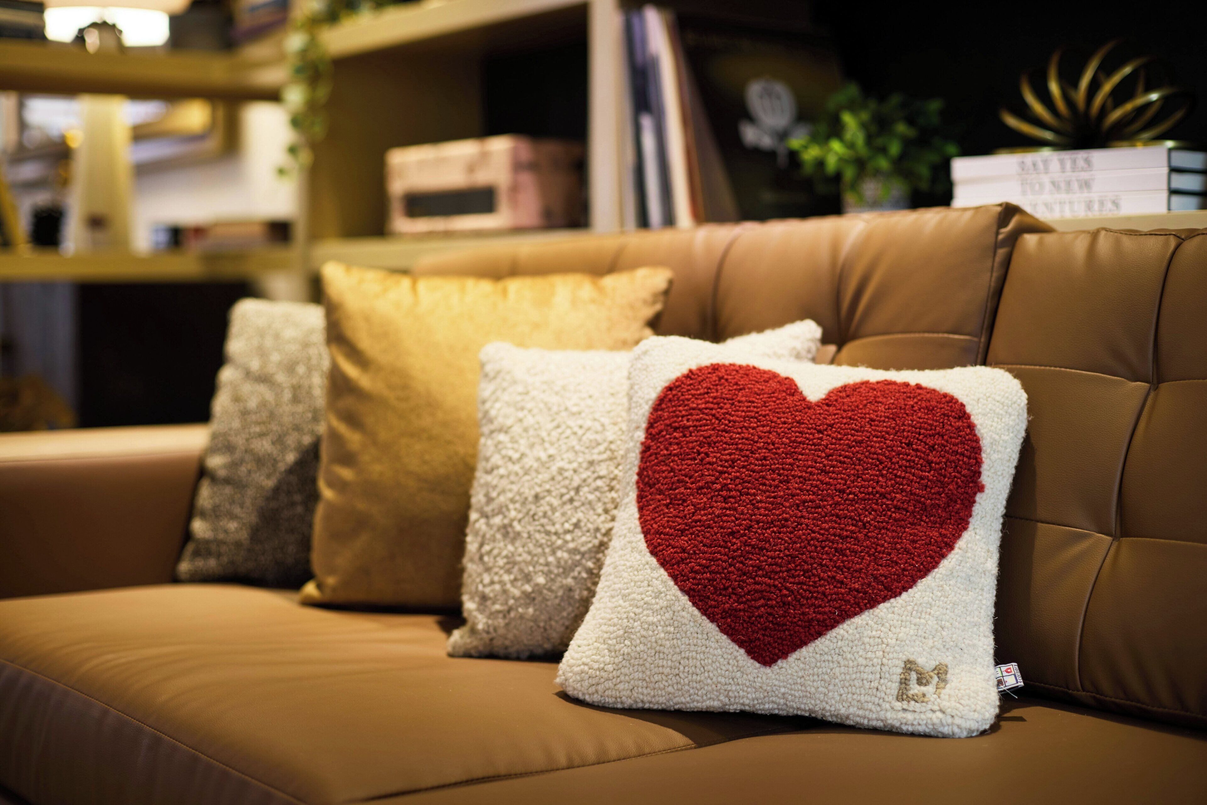 Eine braune Ledersofa mit drei Kissen, eines mit einem roten Herzmuster.