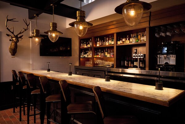 Eine Bar mit einer Marmorplatte, mehreren Barhocker und einer Auswahl an Spirituosenflaschen und Gläsern.