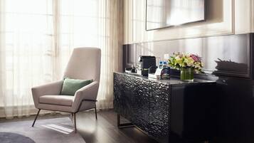 Une chambre d’hôtel moderne, dotée d’un grand téléviseur à écran plat fixé au mur, d’une console sombre au revêtement texturé, d’un fauteuil confortable agrémenté d’un coussin vert et d’un vase de fleurs posé sur la console.
