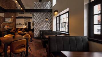 Un restaurante con paredes de ladrillo, papel tapiz estampado y una combinación de asientos de madera y tapizados.