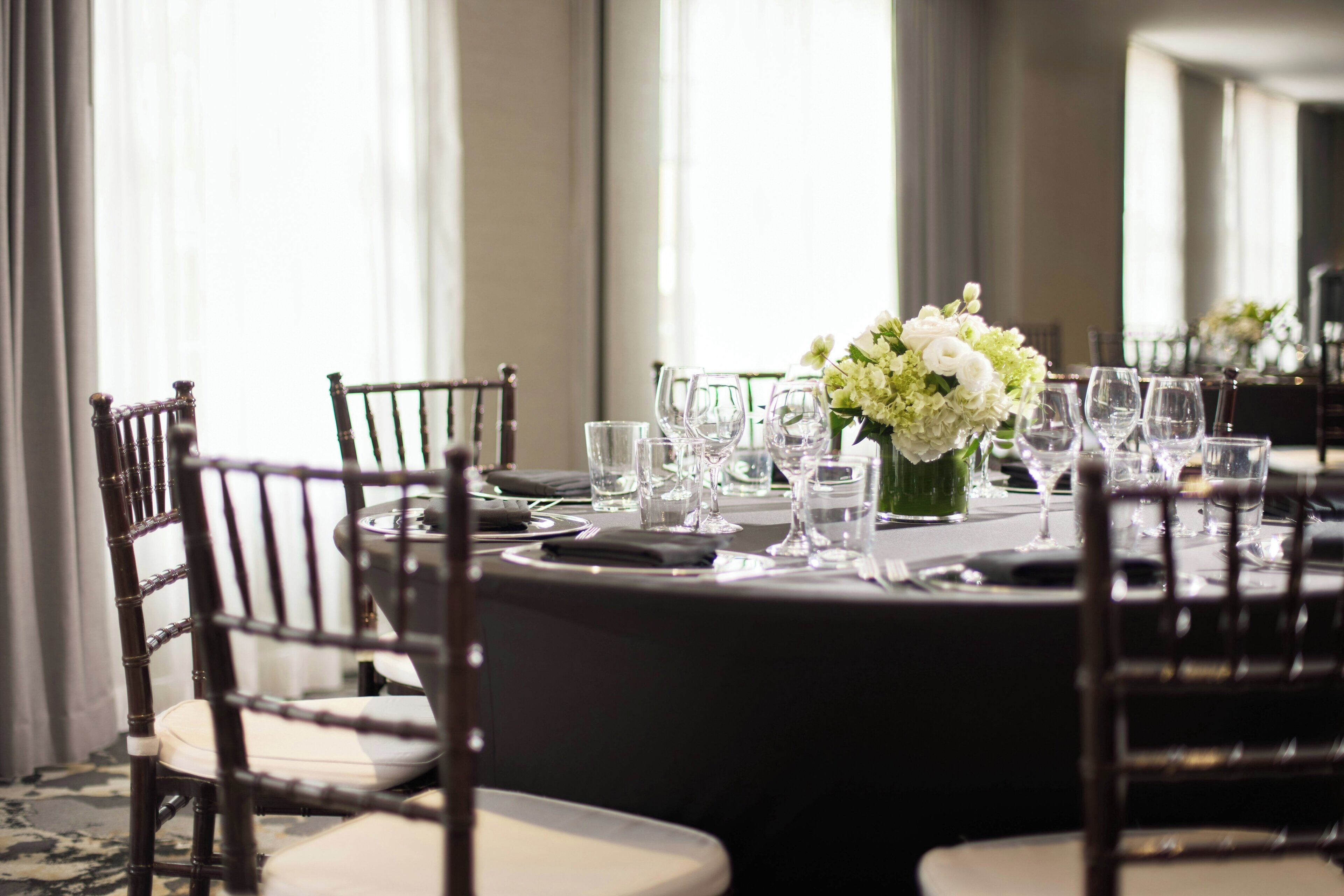 A round dining table with chairs, a vase of flowers, and empty wine glasses.