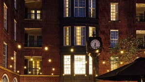 Un bâtiment en briques avec une horloge, des places assises à l’extérieur et une enseigne indiquant « ARCHER HOTEL ».