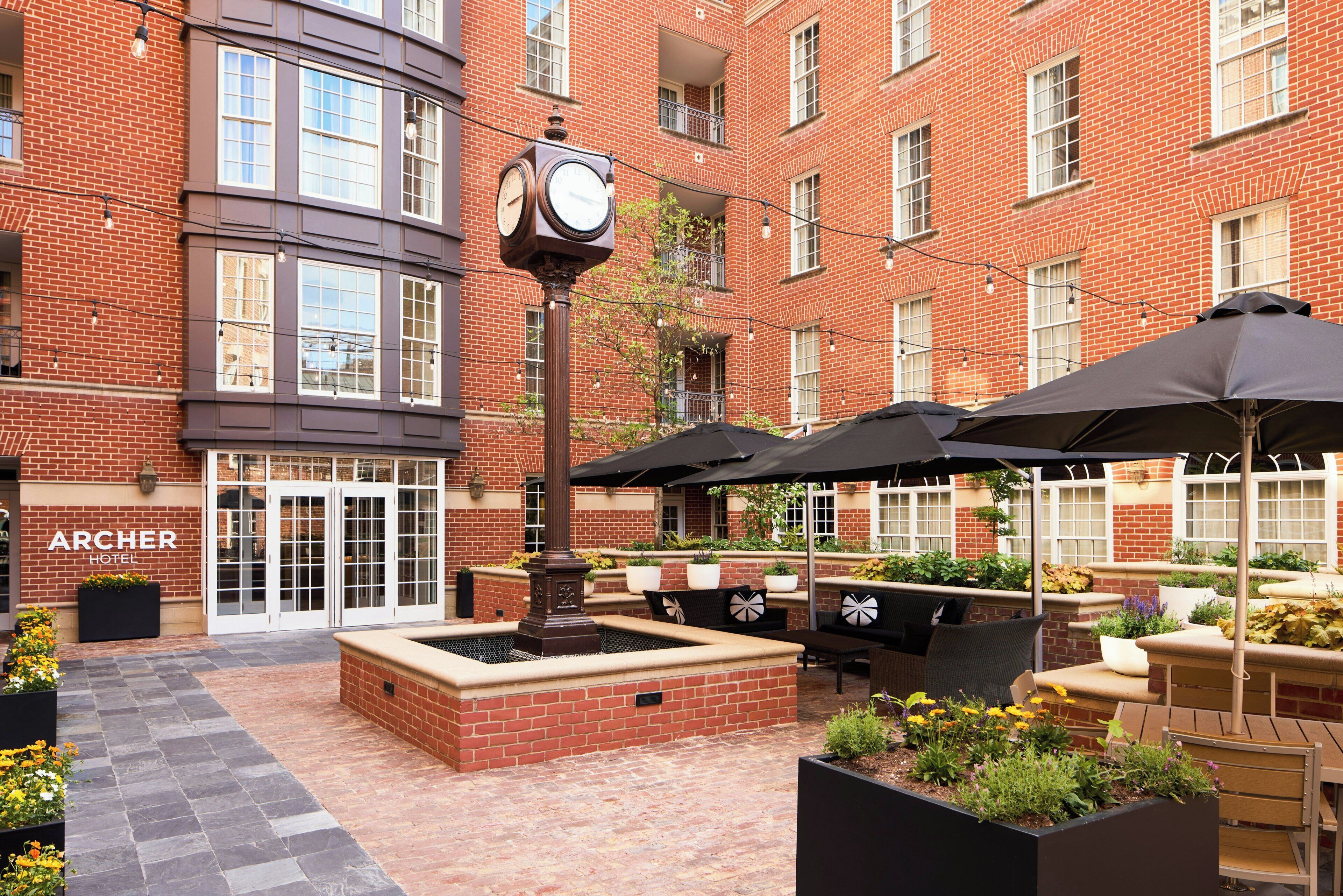 A courtyard with a clock, outdoor seating, and a brick building with a sign reading 'ARCHER HOTEL'.