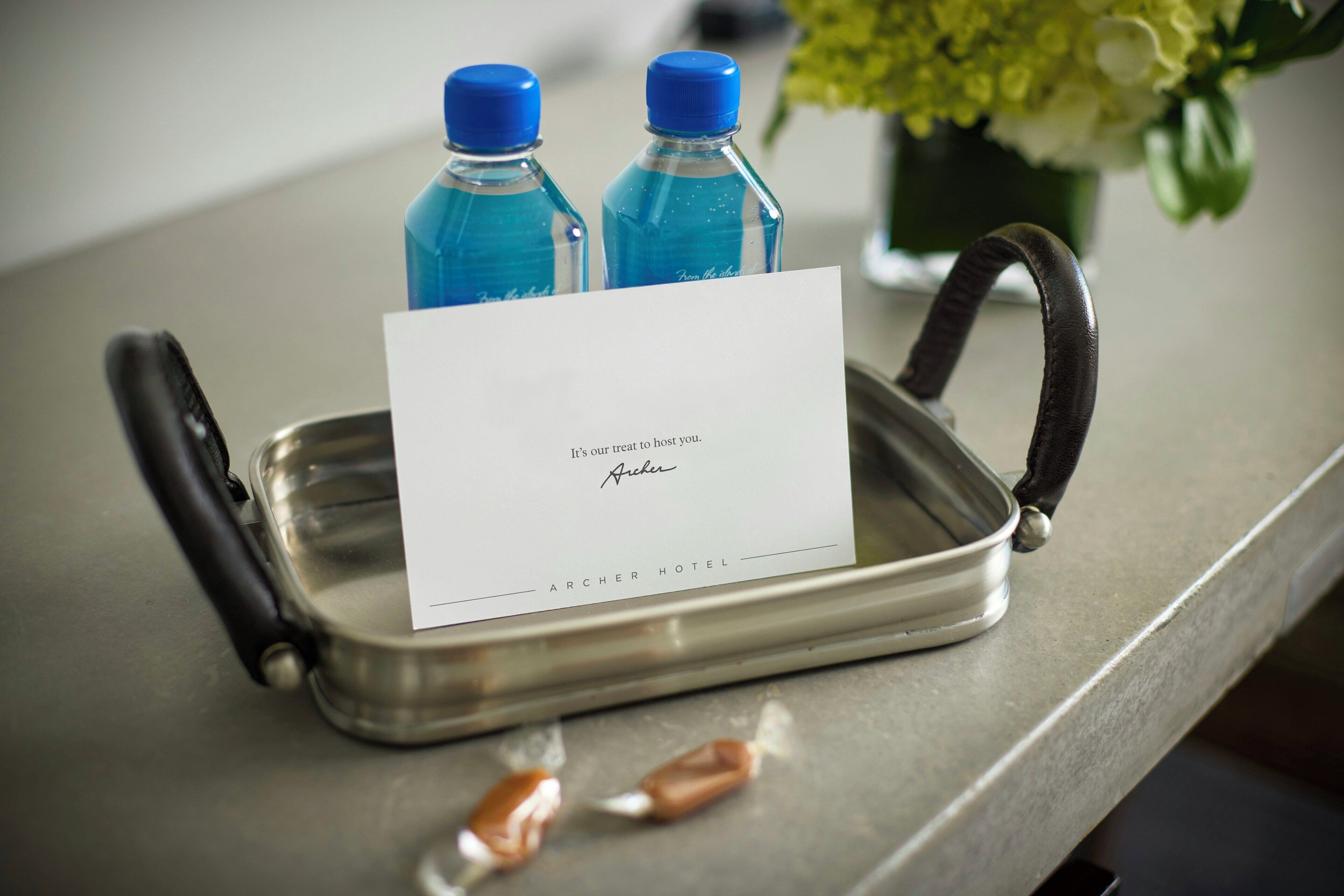 Een dienblad met een kaart, twee waterflesjes en een vaas met bloemen op een hotelbalie.
