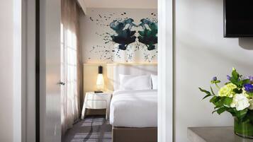 Ein Hotelzimmer mit Bett, Nachttisch mit Lampe, Wand-Fernseher und Blumen in einer Vase.