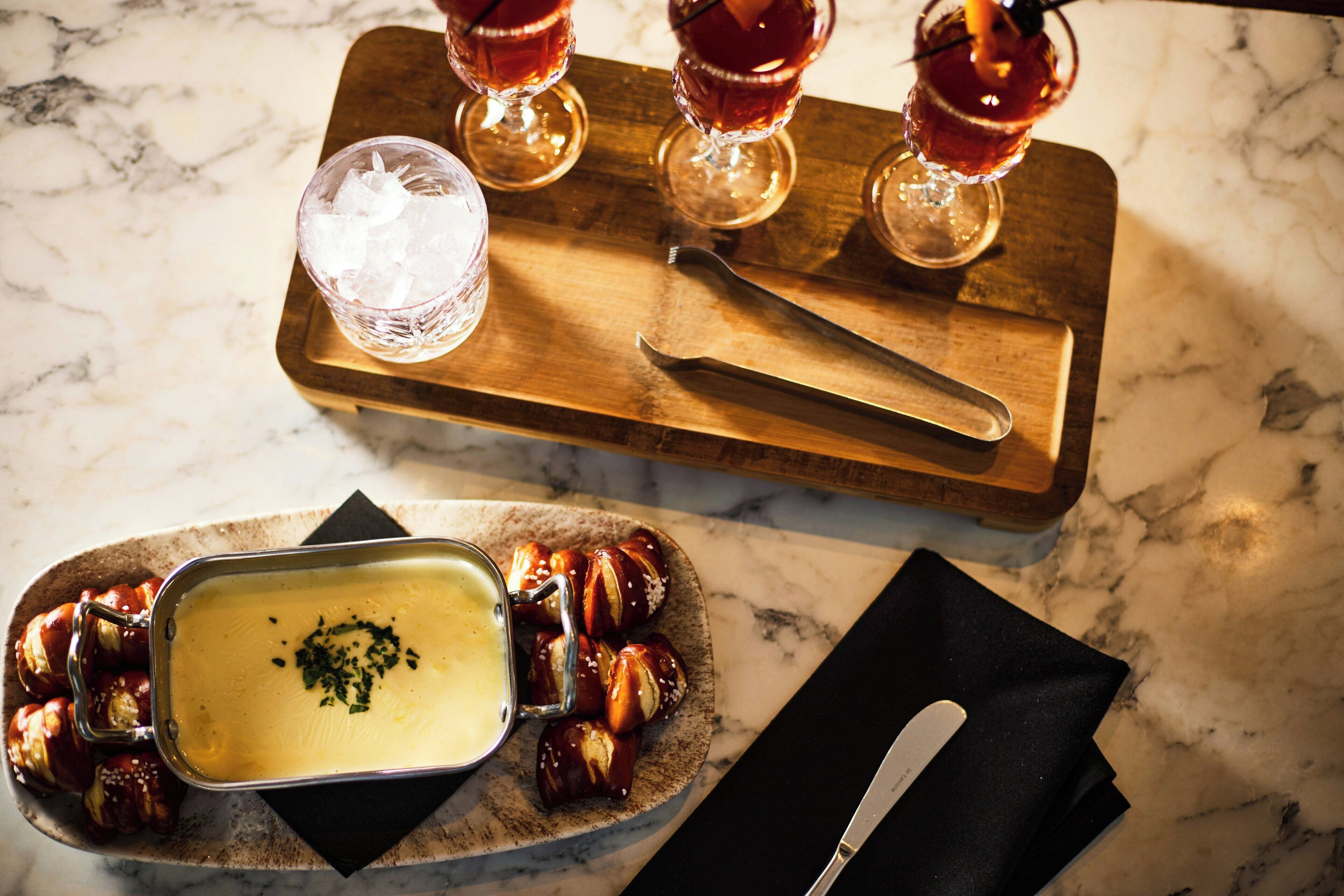 A wooden serving board with a glass of iced beverage, a knife, and a dish of food.