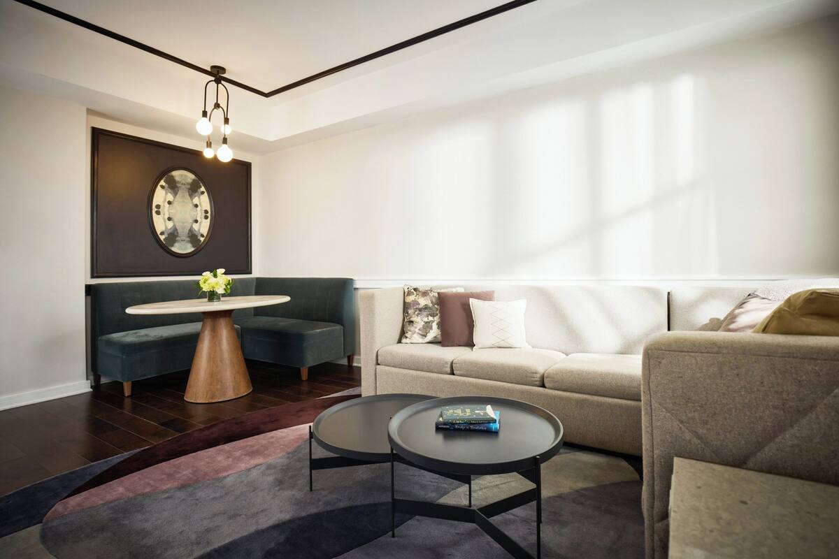 Uma sala de estar moderna com um sofá, duas mesas de centro, uma mesa redonda com flores e um relógio fixado na parede.