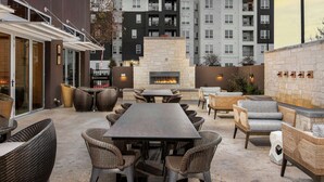 An outdoor patio with a stone fireplace, wicker furniture, and a view of apartment buildings in the background.