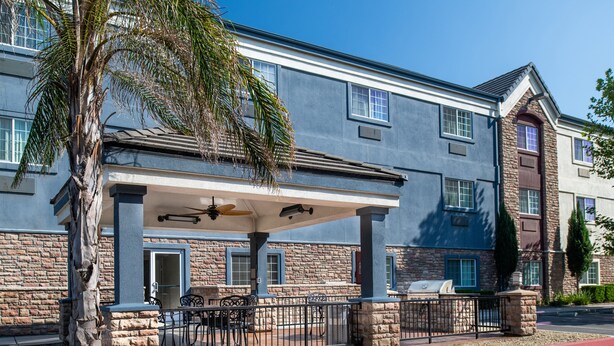 A hotel with a covered patio, outdoor seating, and a stone facade.