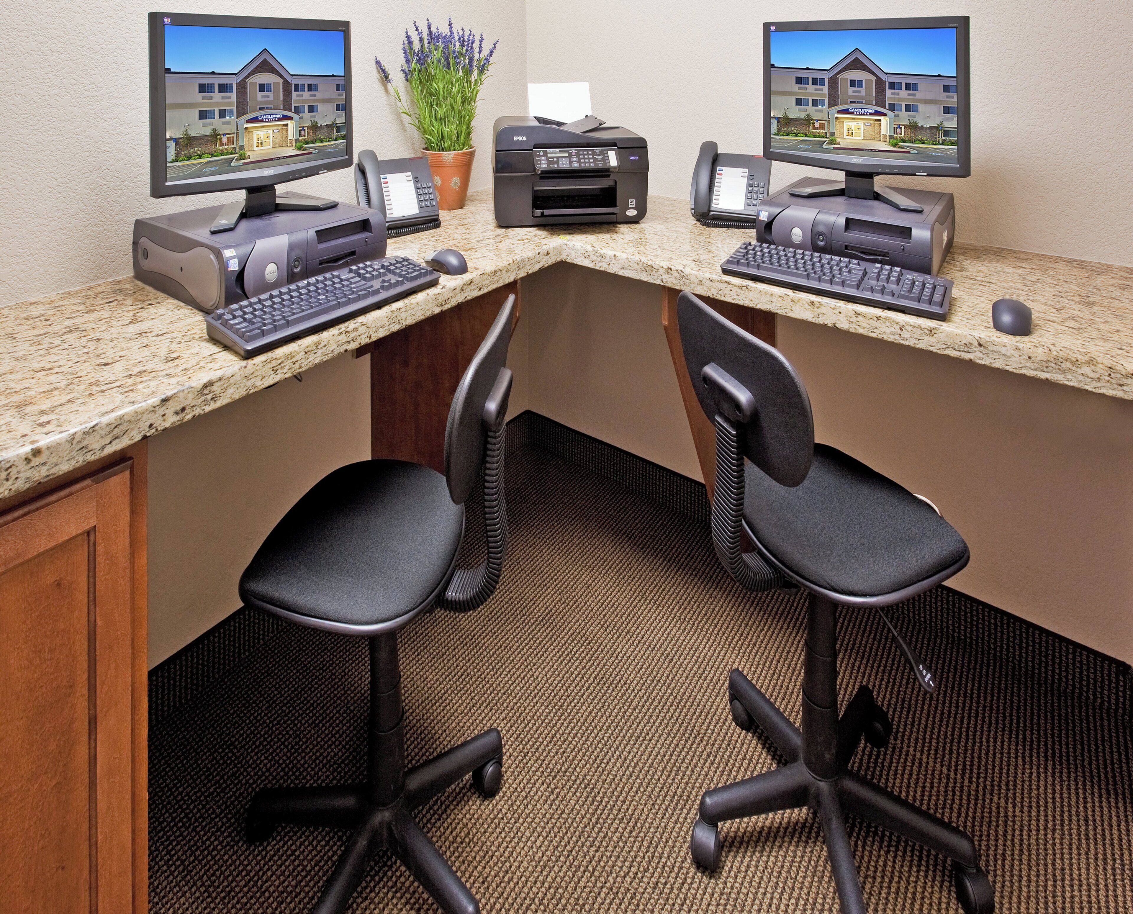 A hotel reception desk with two monitors, a printer, a telephone, and two office chairs.