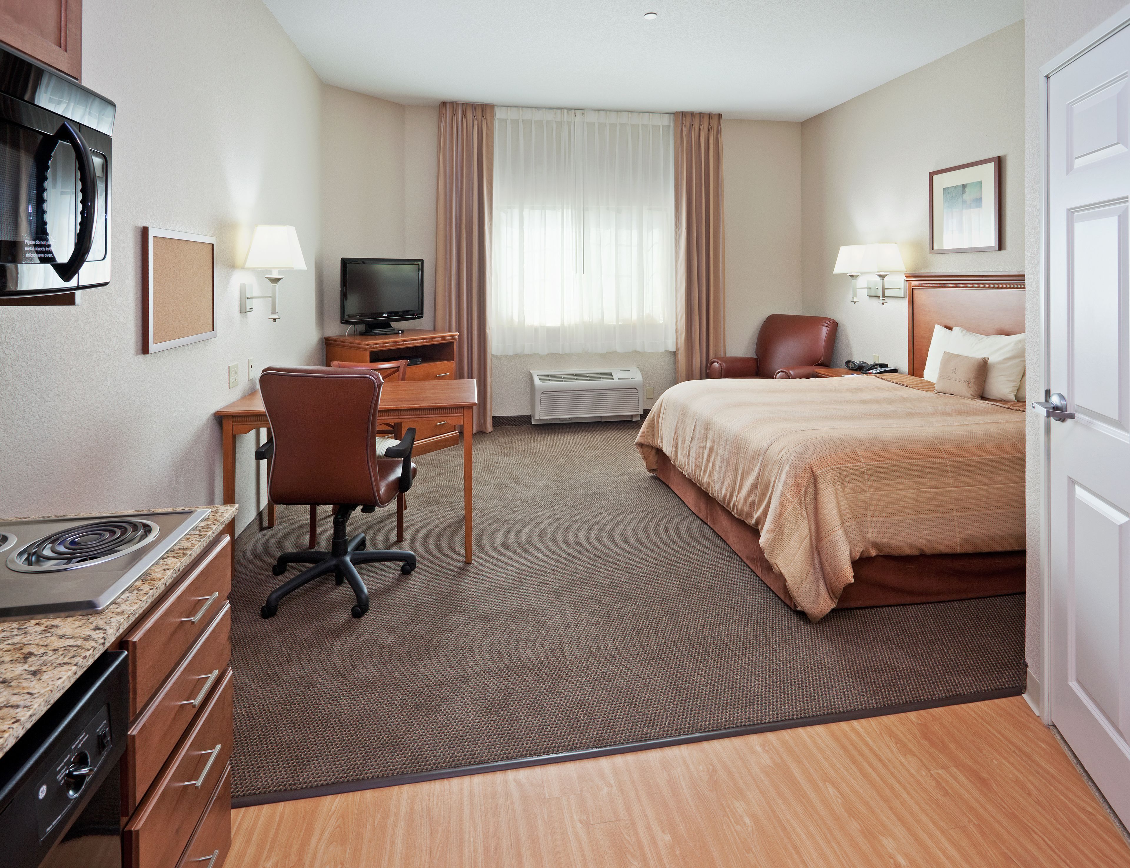 Habitación de hotel con cama, escritorio, silla, televisor, aire acondicionado y microondas.