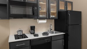 A modern kitchen with black cabinetry, a stainless steel sink, a black refrigerator, and a microwave.