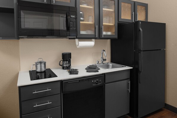 Une cuisine moderne avec des meubles de rangement noirs, un évier en acier inoxydable, un réfrigérateur noir et un four à micro-ondes.