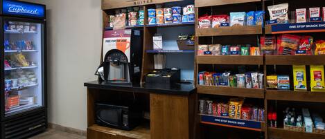 Una tienda de snacks con una variedad de productos, bebidas, una máquina de café y un refrigerador.
