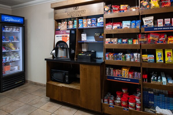 Una tienda de snacks con una variedad de productos, bebidas, una máquina de café y un refrigerador.