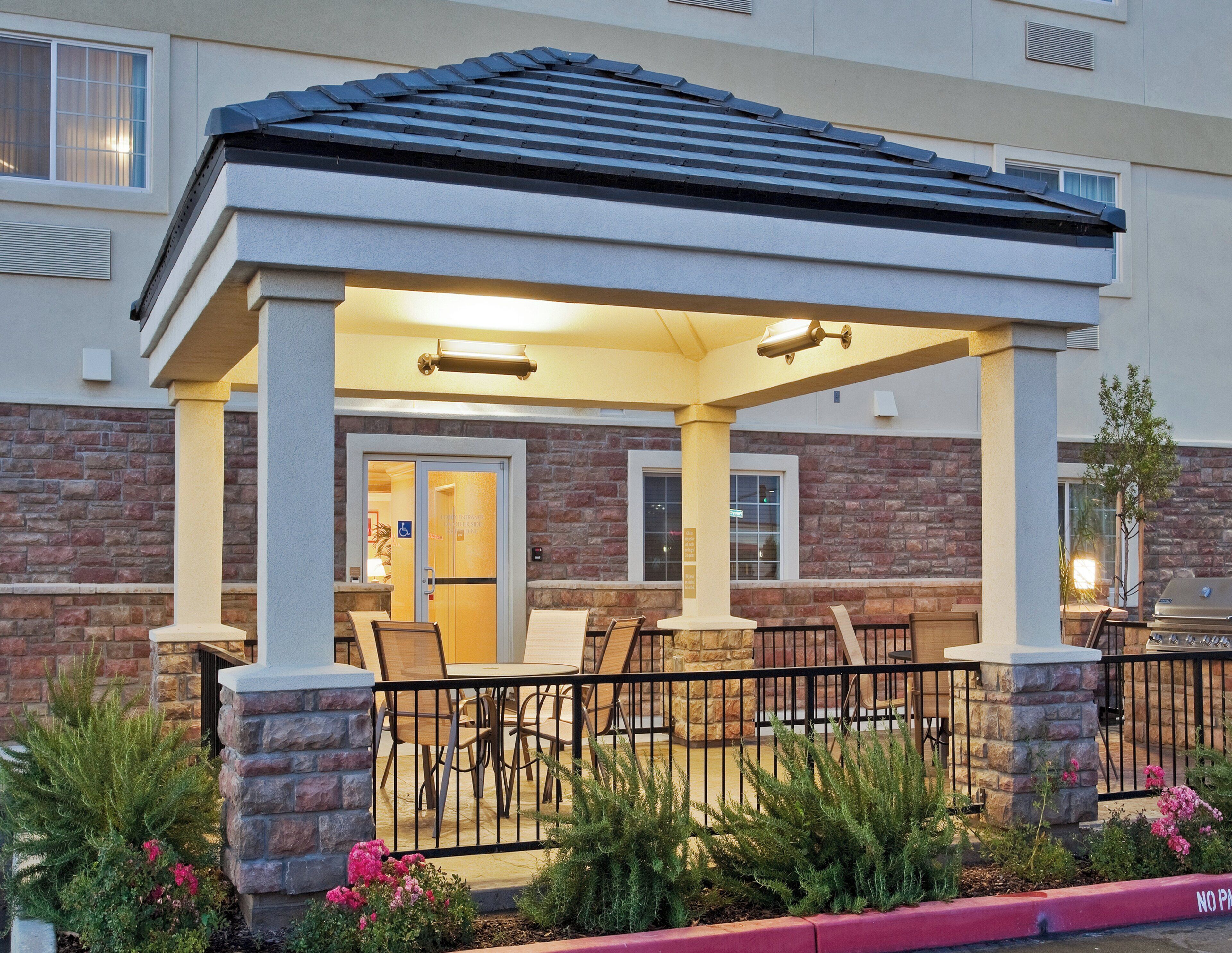 A covered outdoor seating area with a patio table and chairs, a stone pillar, and a brick wall.