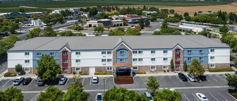 A hotel with a central entrance, multiple parking lots, and surrounding greenery.