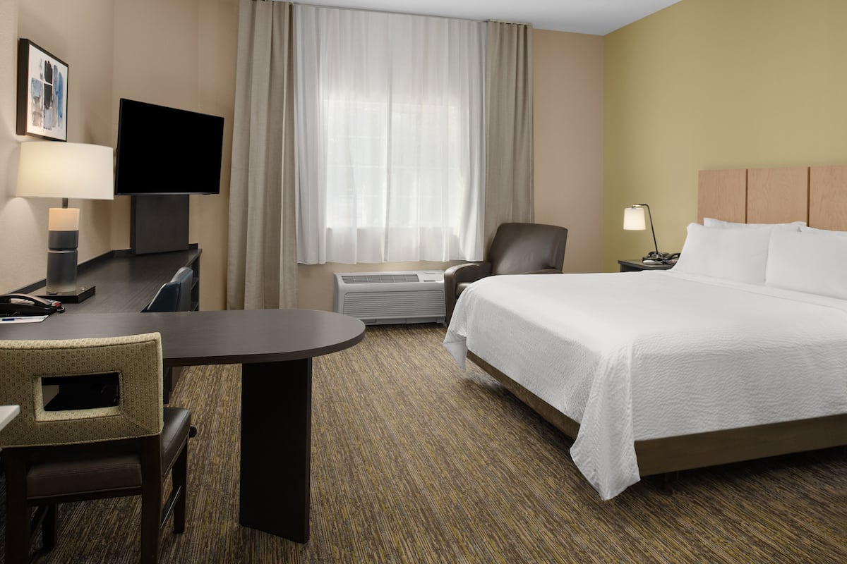 A hotel room with a bed, a desk, a chair, a television, and a window with curtains.