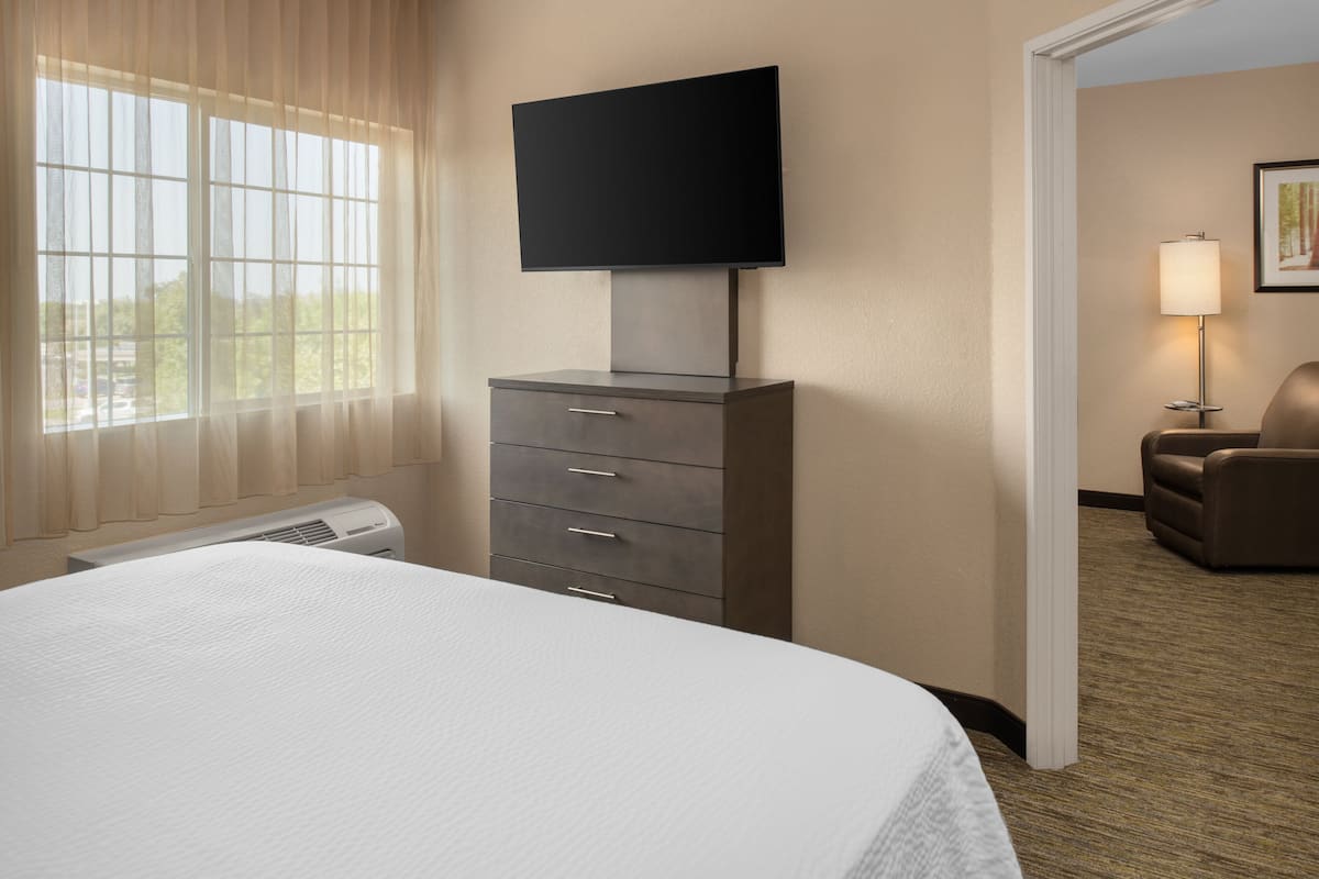 A hotel room with a bed, a television mounted on a dresser, a chair, and a lamp.