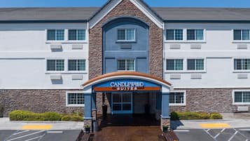 Entrada de hotel com fachada de pedra, toldo azul e laranja e estacionamento com vagas demarcadas.