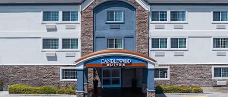 A hotel entrance with a stone facade, a blue and orange awning, and a parking lot with marked spaces.