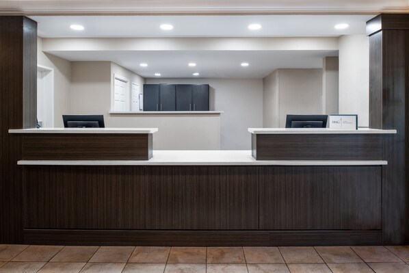 A reception desk with two counters, a dark wood finish, and a tiled floor. - Candlewood Suites Turlock by IHG (Turlock)