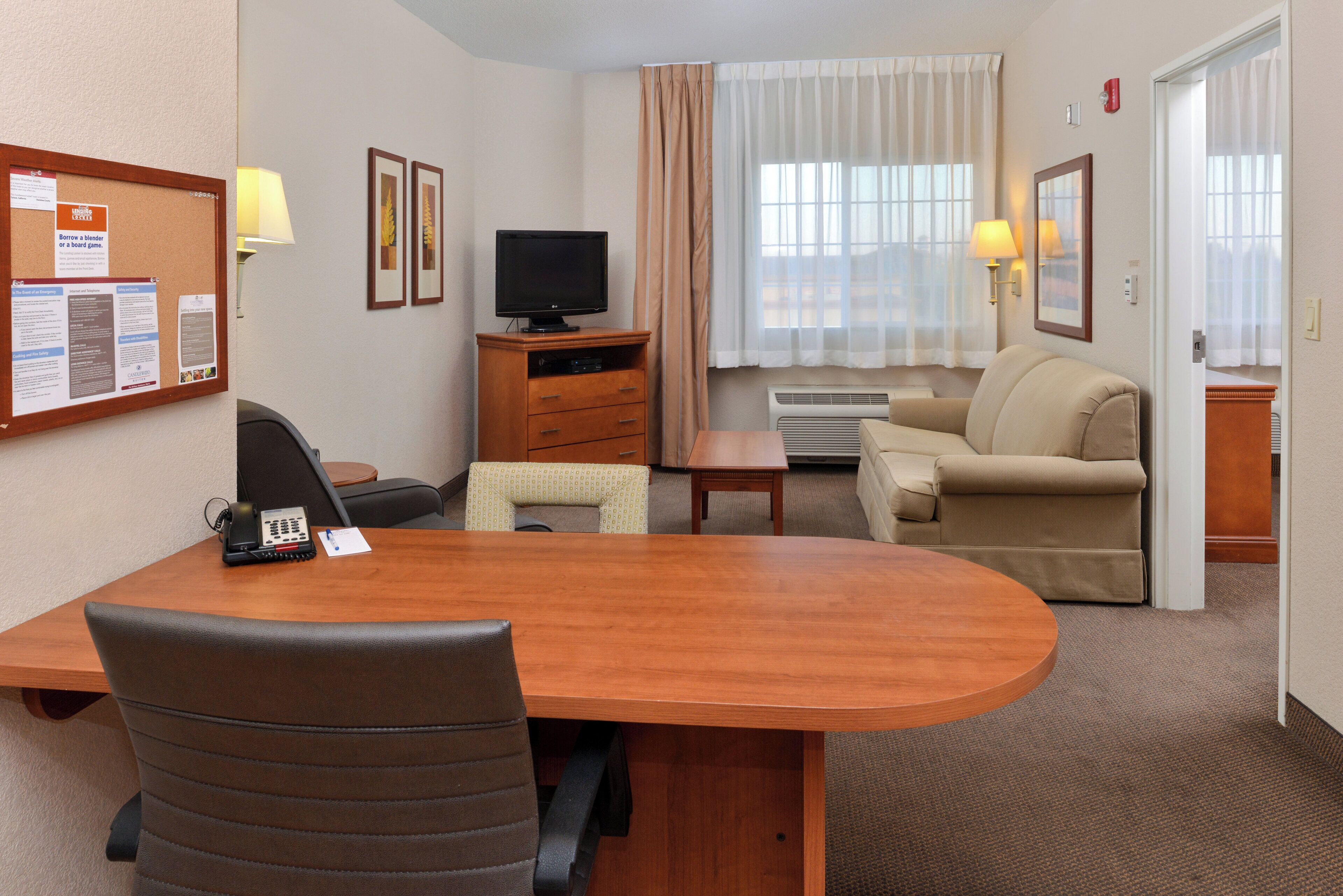 A hotel room with a wooden desk, two chairs, a television, a sofa, and a small table.