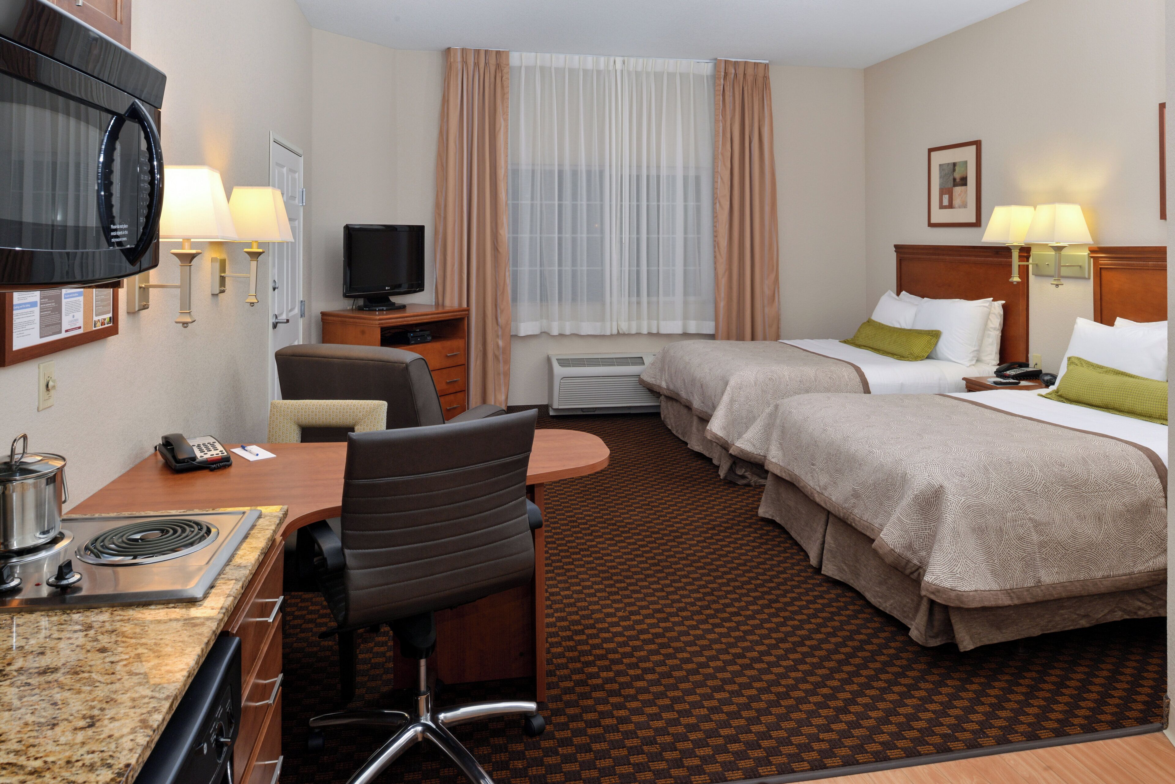 A hotel room with a desk, chair, bed, television, and a window with curtains.