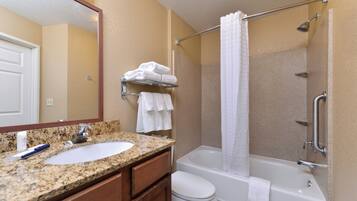 A bathroom with a granite countertop sink, a white toilet, a bathtub with a shower curtain, and a towel rack with folded towels.
