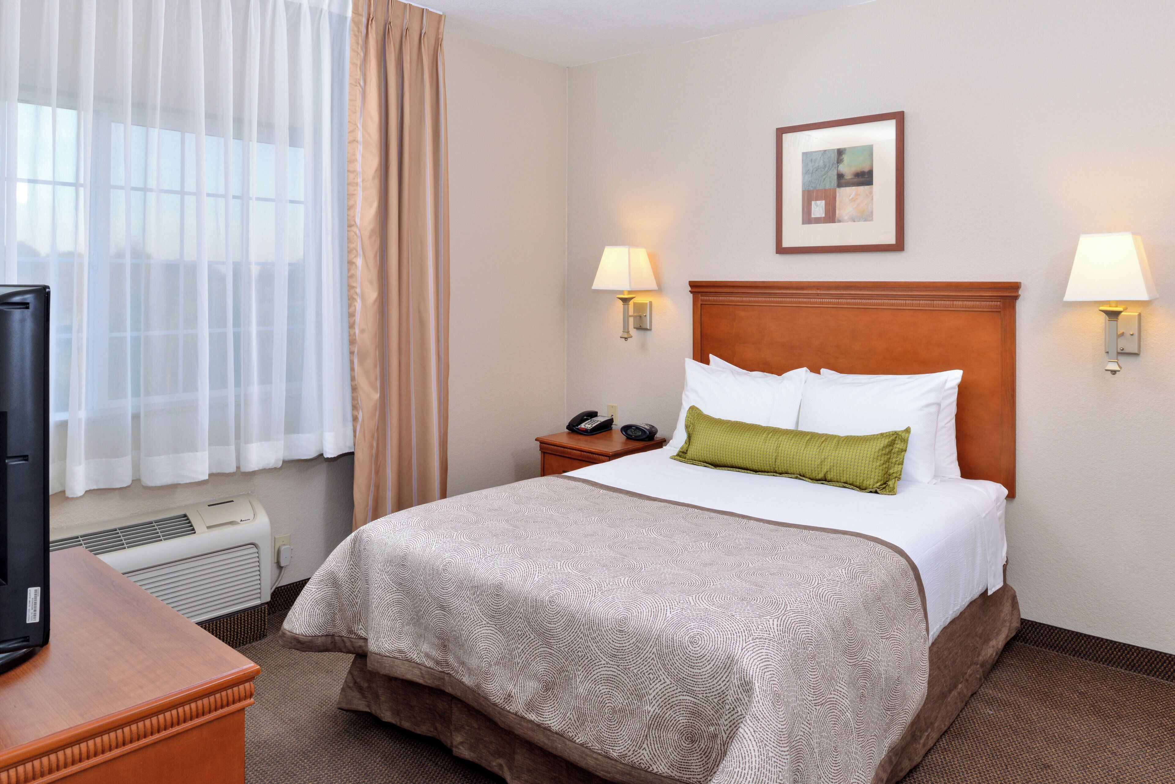 A hotel room with a bed, two bedside lamps, a telephone, a picture on the wall, and a window with curtains.