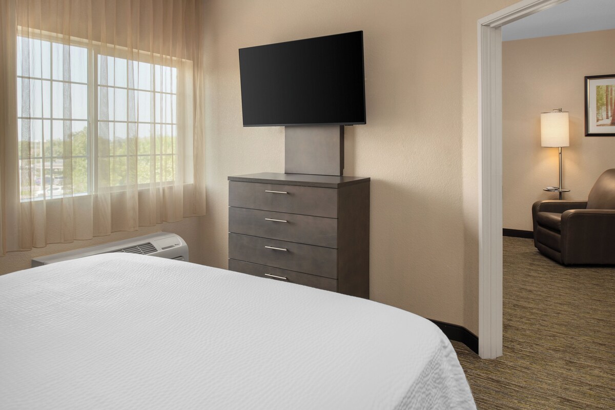 Une chambre d’hôtel avec un lit, un téléviseur fixé à une commode, une chaise et une lampe.