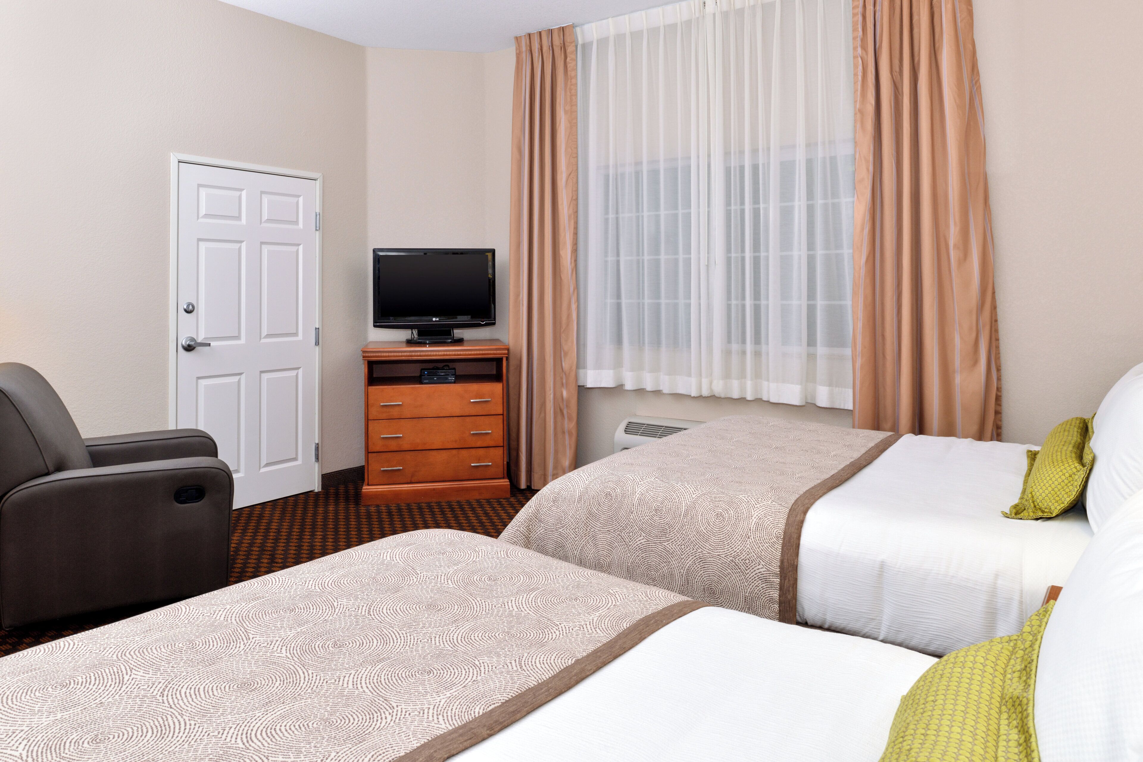 A hotel room with two beds, a television, a dresser, and a door.