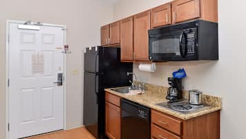Una cocina compacta con armarios de madera, un refrigerador negro, un microondas, una cafetera y un lavavajillas.