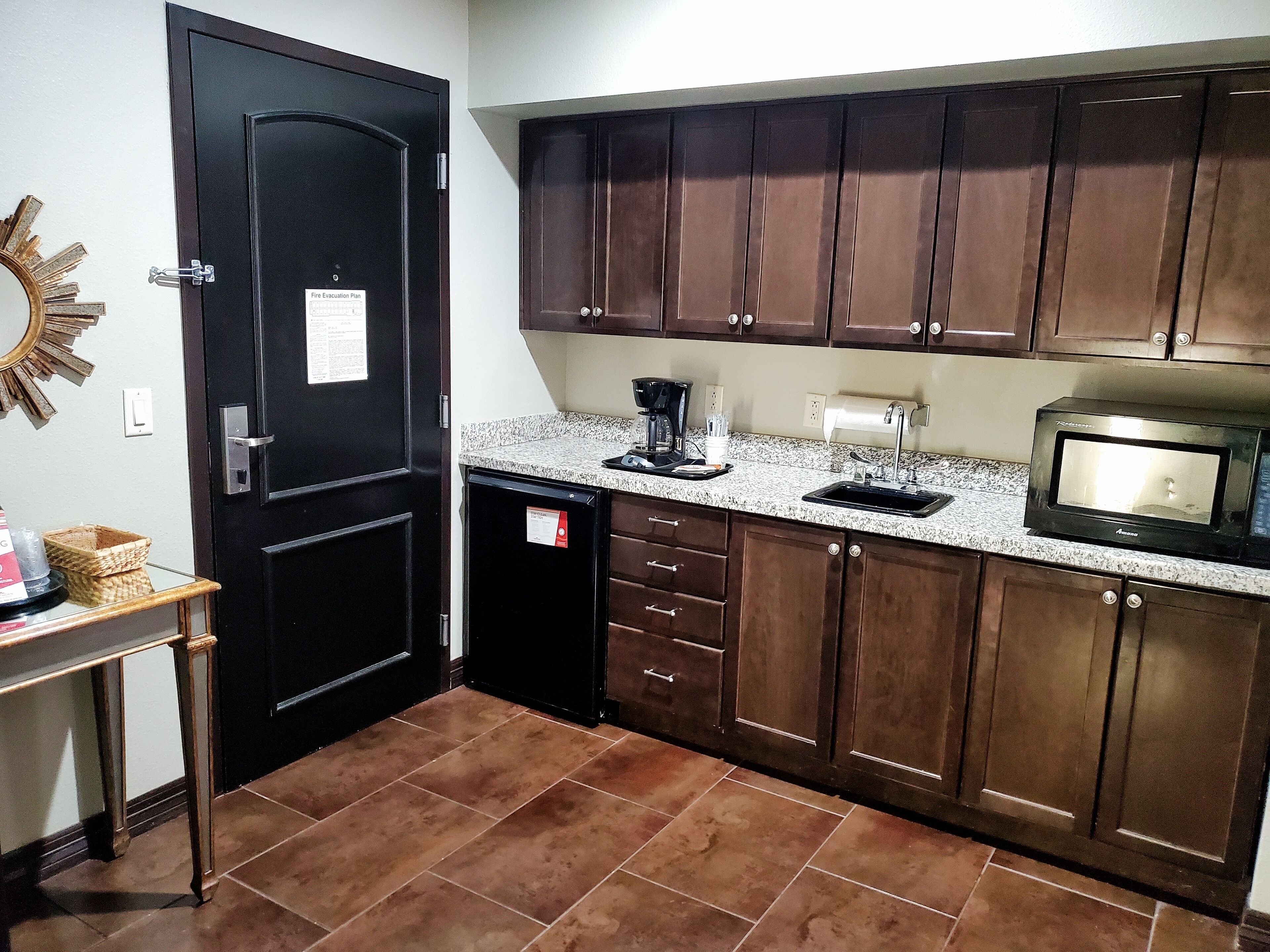 A compact kitchen with dark wooden cabinets, a granite countertop, a black refrigerator, a microwave, and a coffee maker.