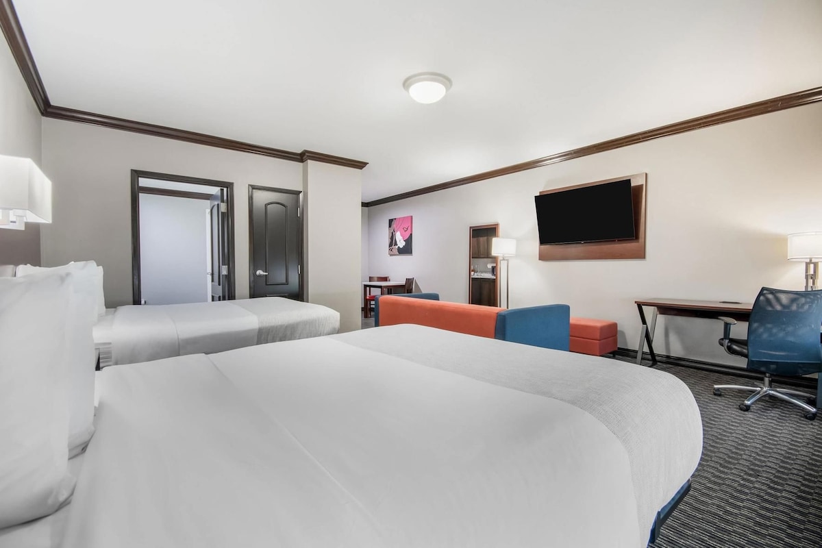 A hotel room with two beds, a desk, a chair, a TV, and a door.