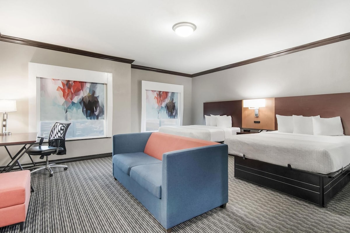 A hotel room with a large bed, a sofa, a desk with a chair, and artwork on the walls.