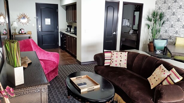 Een woonkamer met een bruine bank, een rode fauteuil, een salontafel en een keuken op de achtergrond.