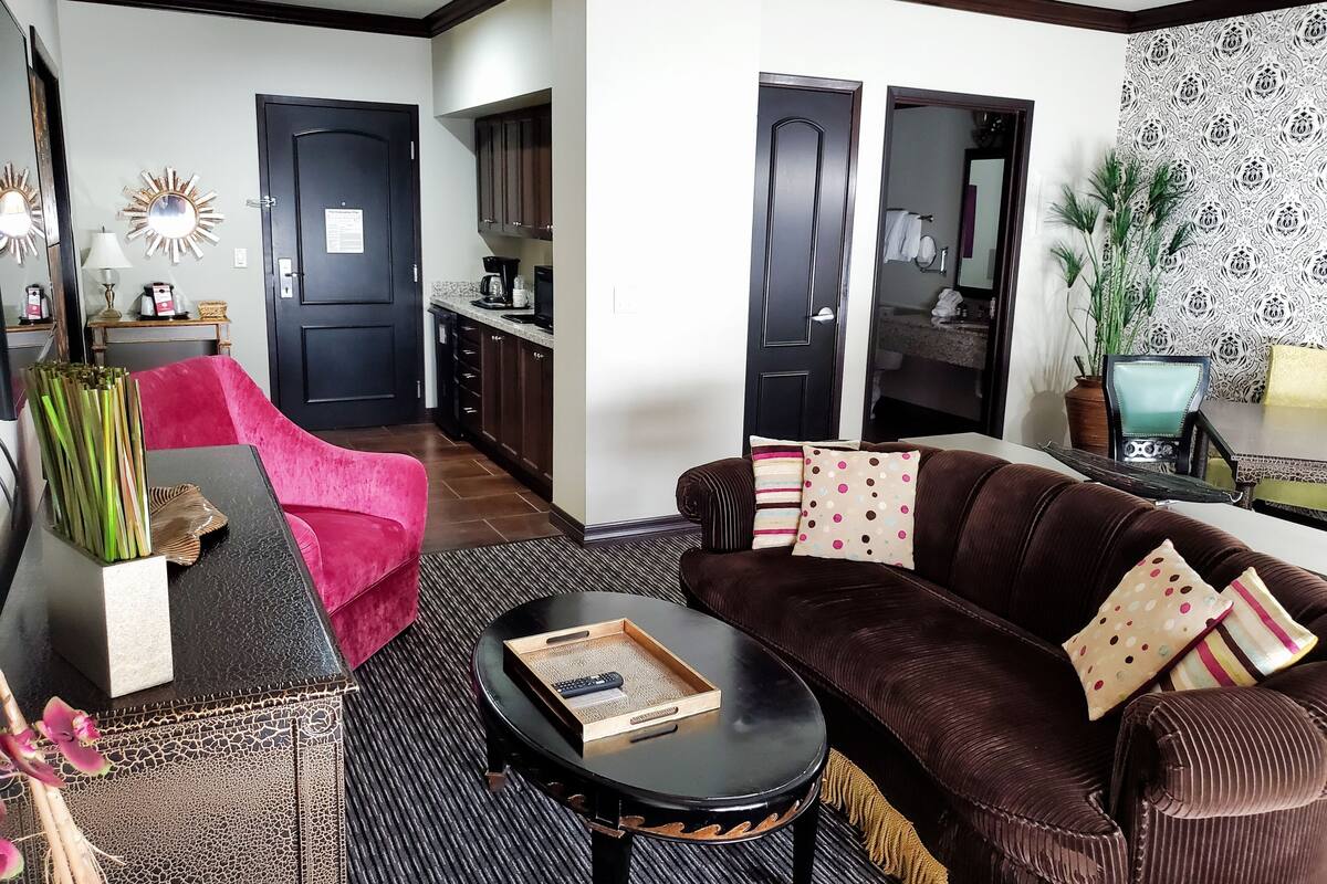 Ein Wohnzimmer mit einem braunen Sofa, einem roten Sessel, einem Couchtisch und einer Küche im Hintergrund.