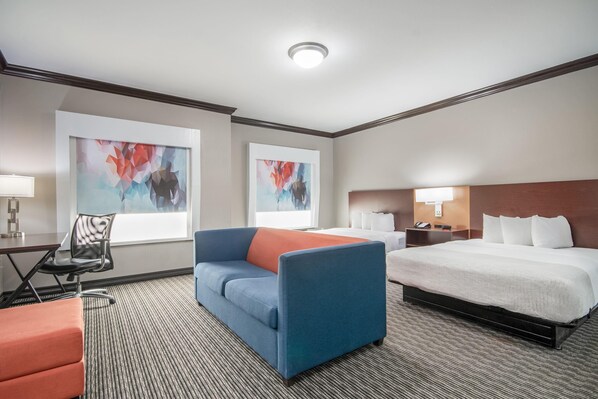 Una habitación de hotel con cama, sofá, escritorio y dos cuadros abstractos en las paredes.
