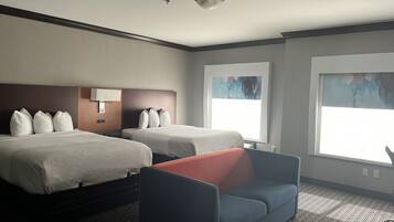 Una habitación de hotel con dos camas, un sofá y ventanas amplias.