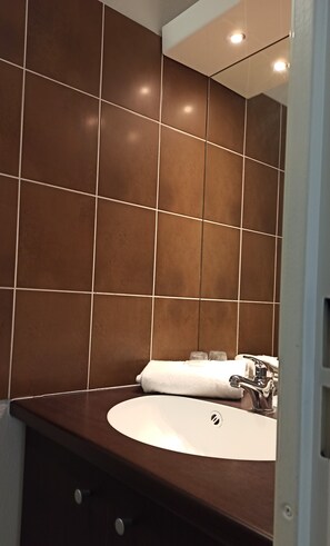 Une salle de bain avec des carreaux marron, un lavabo blanc et un miroir.