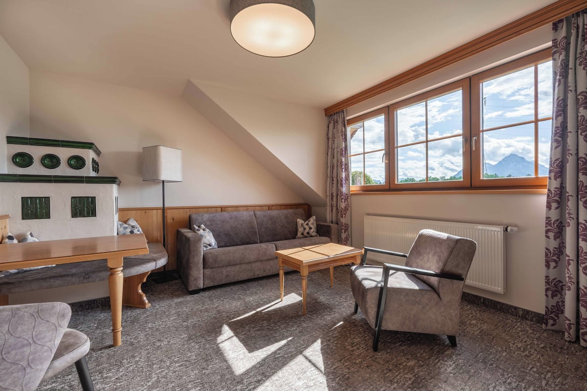 Una habitación acogedora con sofá, sillón, mesa y ventana con vistas a montañas.